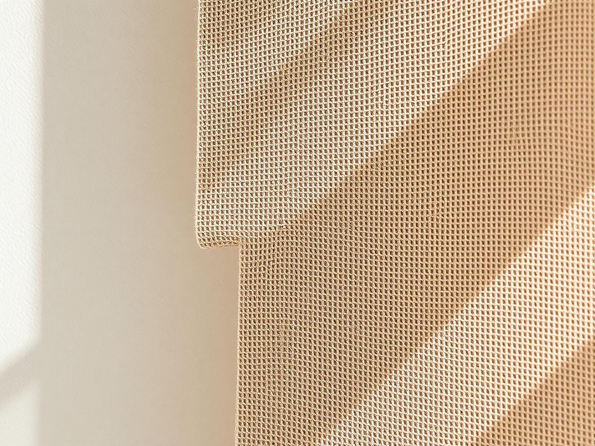 Detail of a stretched fabric wall panel edge with woven sand-toned fabric